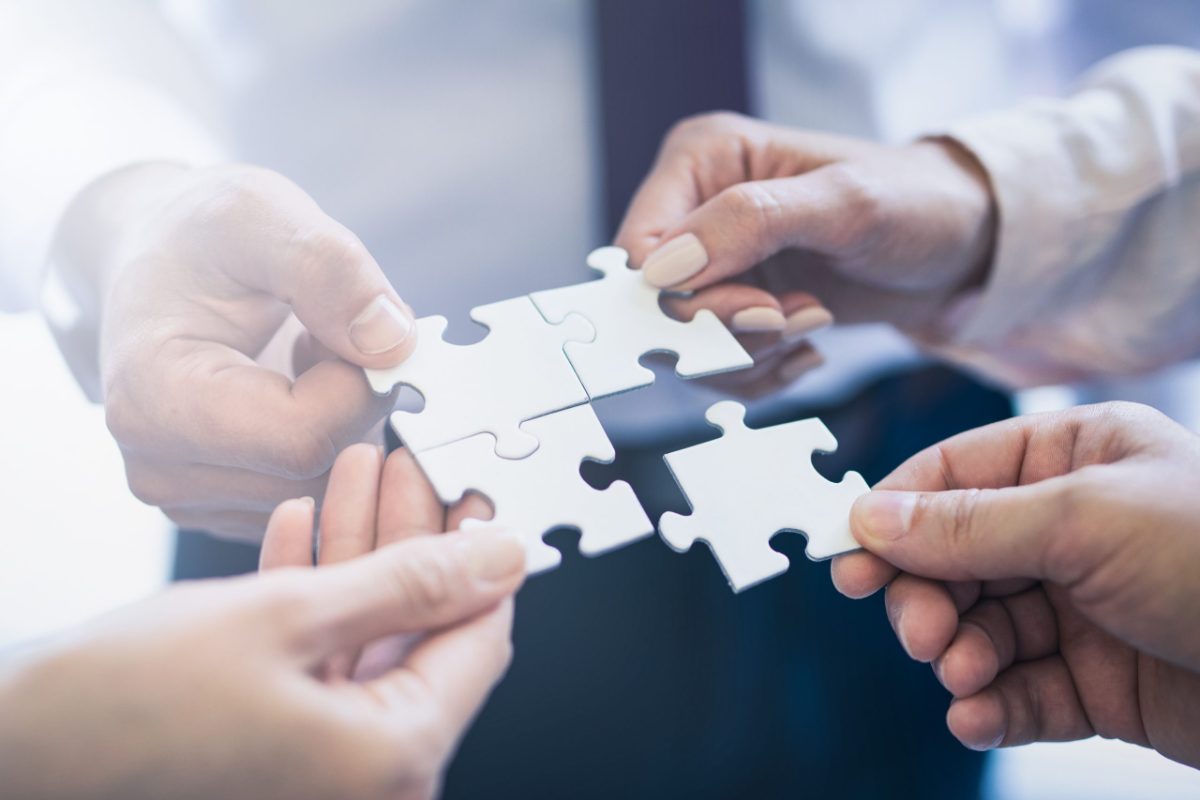 Four hands joining puzzle pieces together